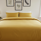 Yellow bedspread on a bed in a well-lit bedroom with framed art on the wall.