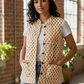 Woman wearing a floral patterned vest indoors with large windows and plants.