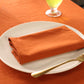 Orange napkin on a white plate with a gold fork on an orange tablecloth.