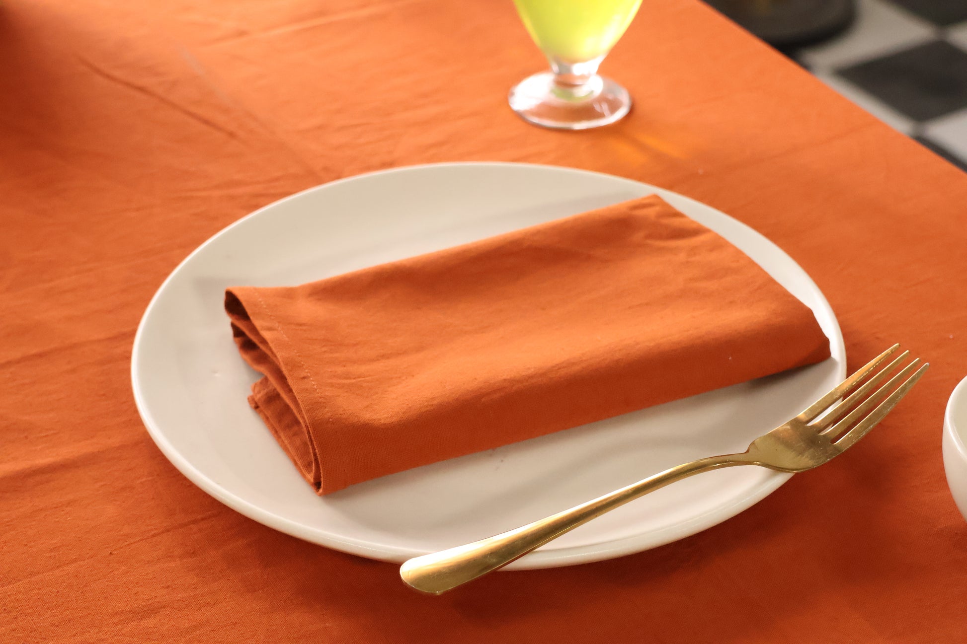 Orange napkin on a white plate with a gold fork on an orange tablecloth.