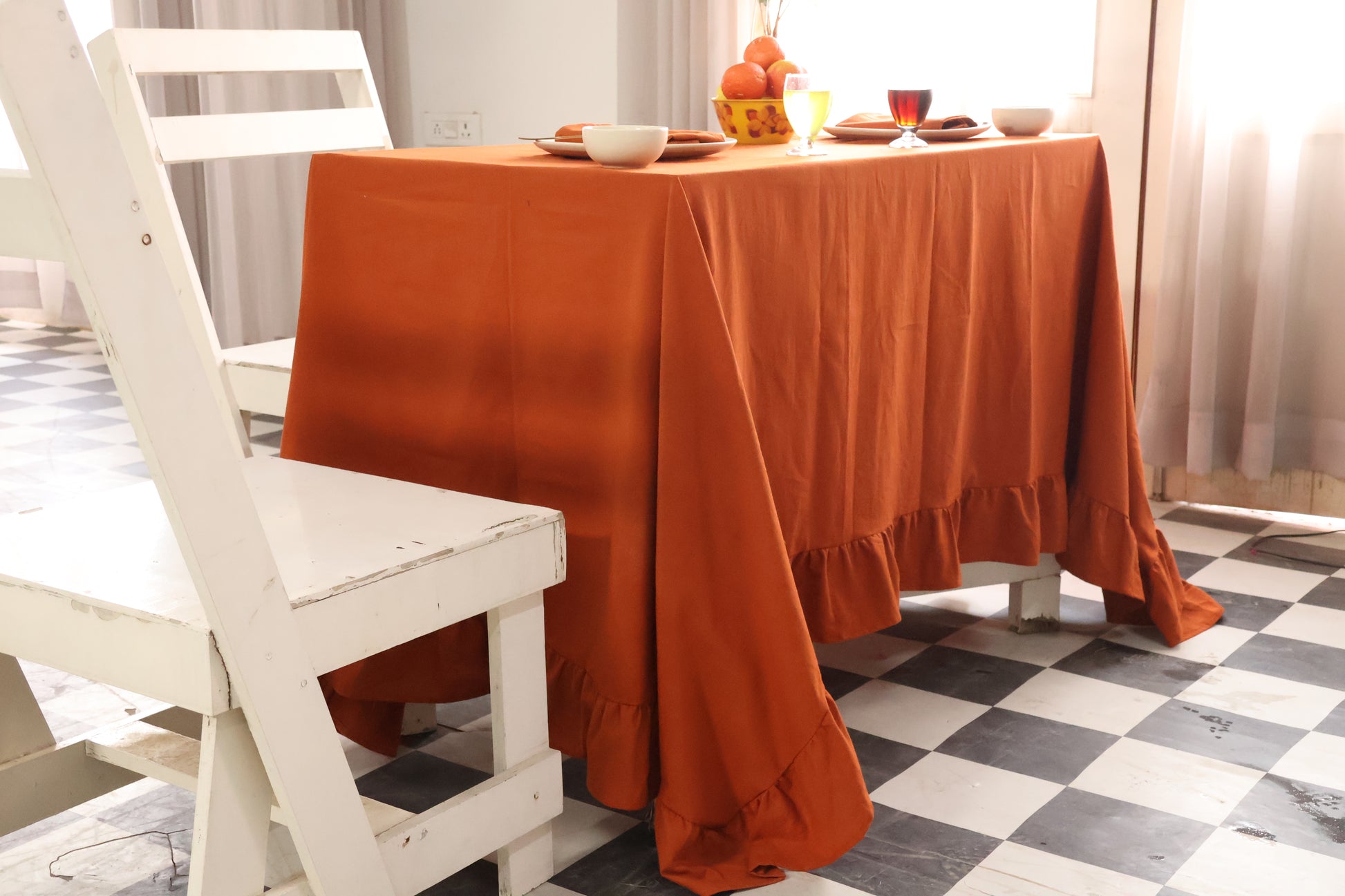 Dining table with an orange tablecloth, white chairs, and a checkered floor.