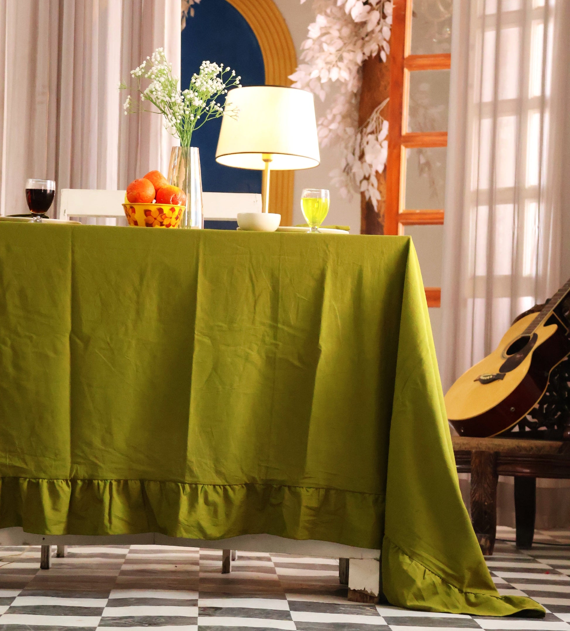 Green tablecloth on a table with decorative items in a room with a guitar and floral decorations.