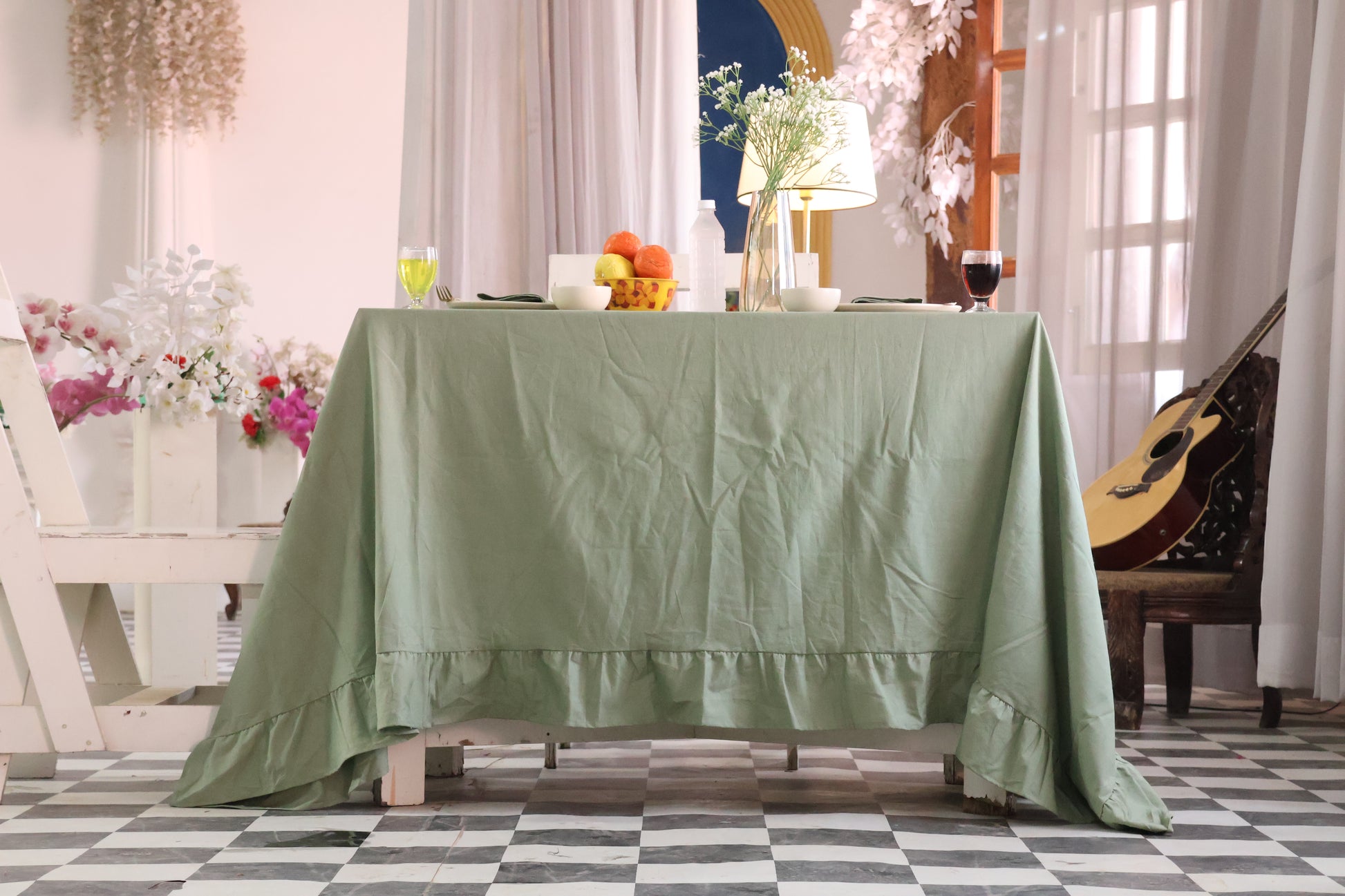 sage Green tablecloth on a wooden table with decorative items in a room with checkered floor and curtains.
