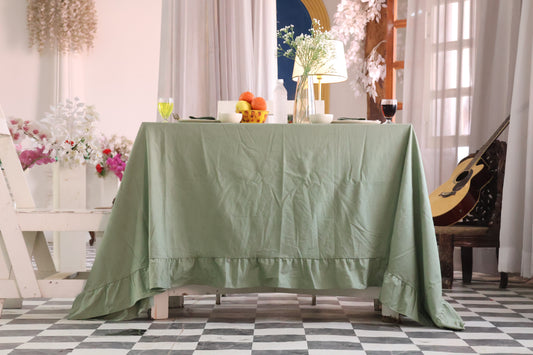 sage Green tablecloth on a wooden table with decorative items in a room with checkered floor and curtains.