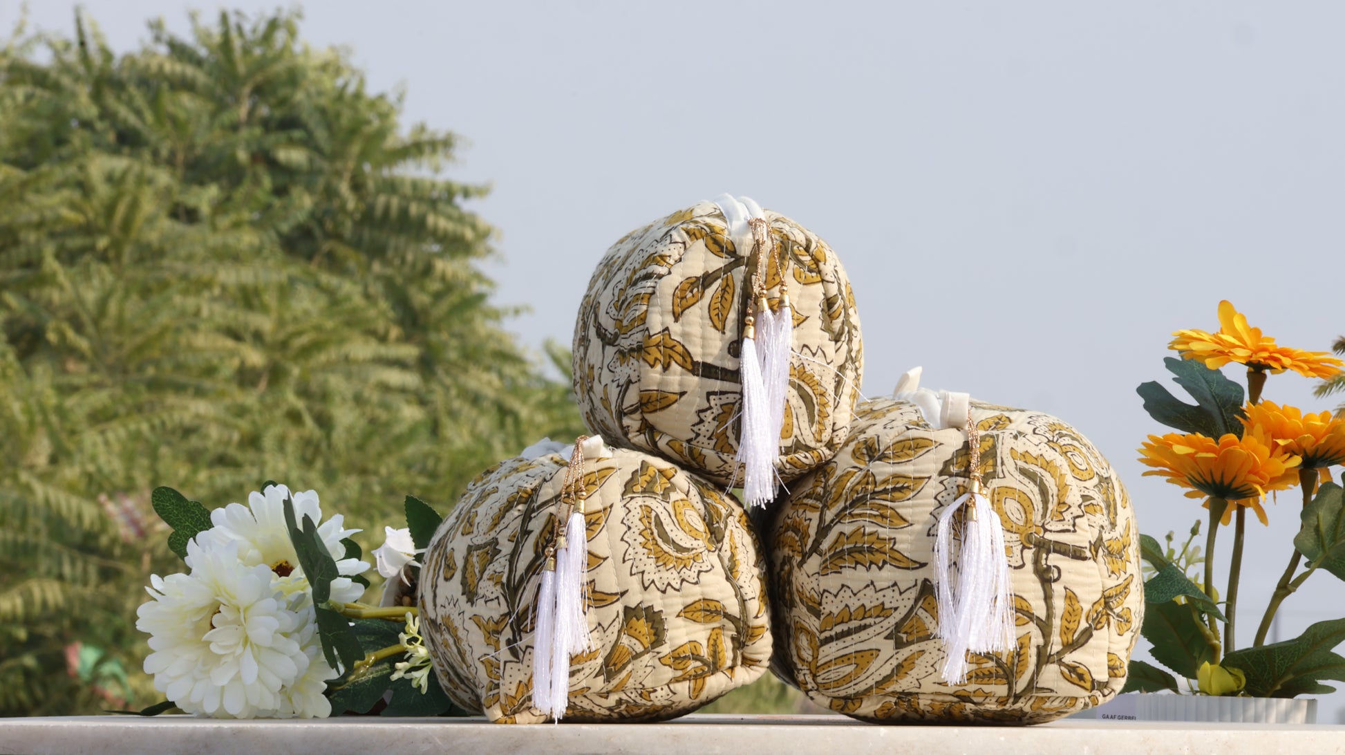 Three patterned balls with ribbons on a surface with flowers and greenery in the background