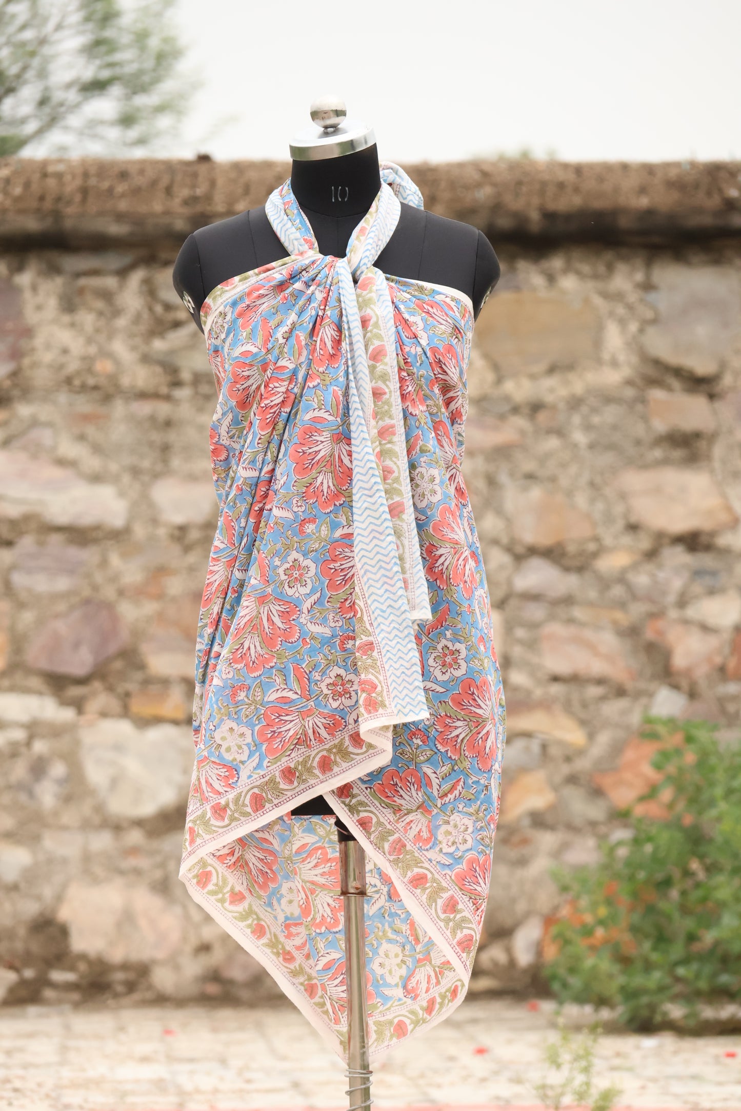 Handblock printed cotton sarong with coral floral design on blue background displayed on mannequin outdoors