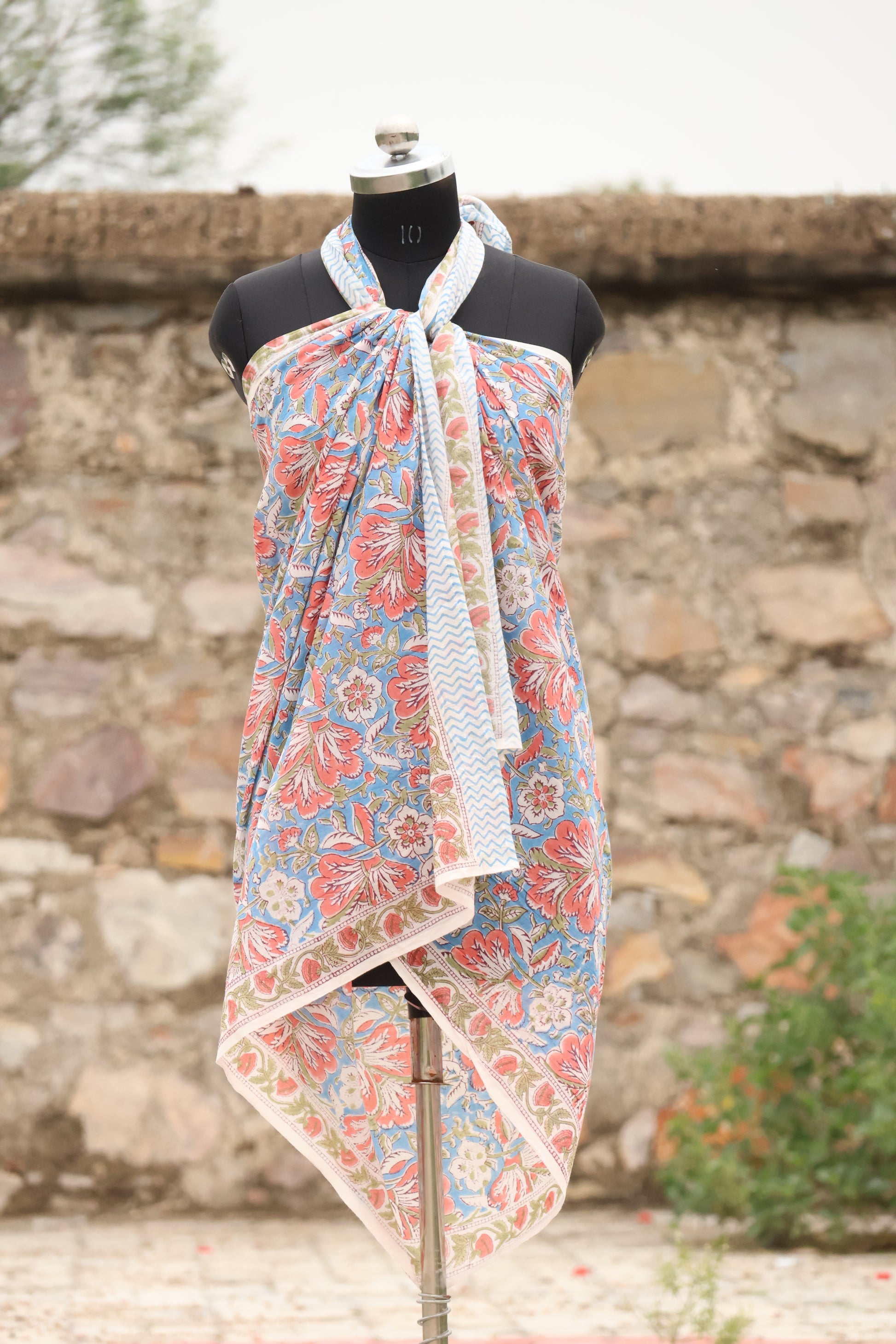 Handblock printed cotton sarong with coral floral design on blue background displayed on mannequin outdoors
