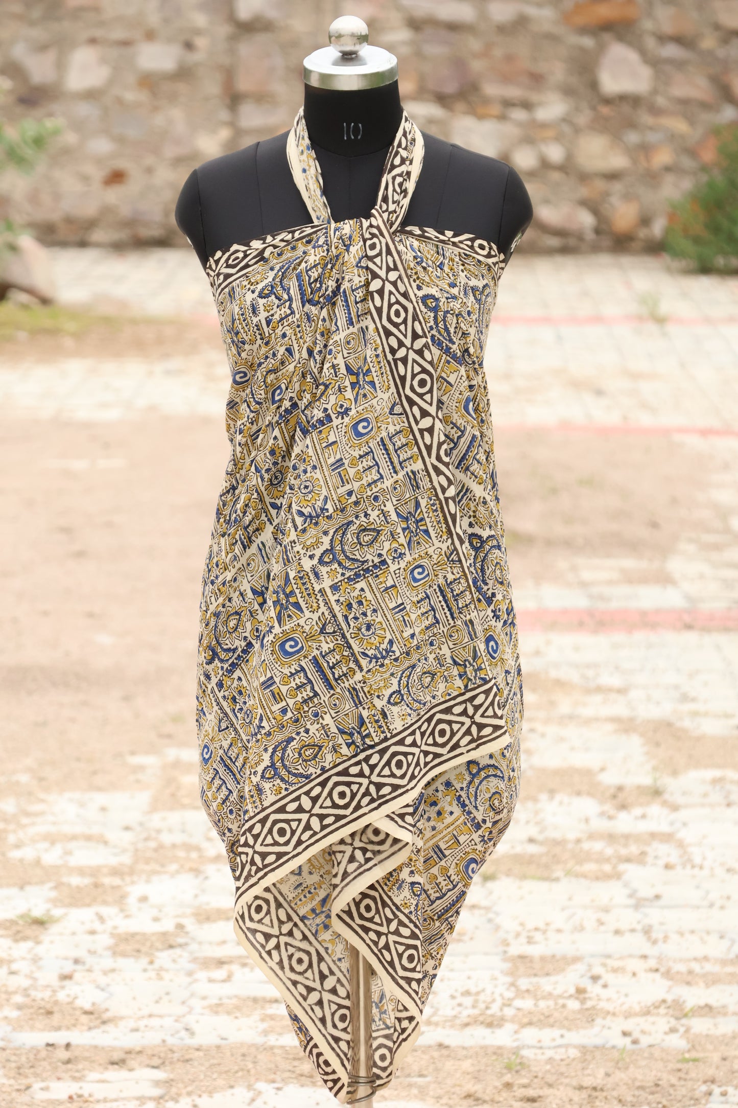 Handblock printed cotton sarong with tribal and geometric motifs in mustard, blue, and black, displayed on a mannequin outdoors.