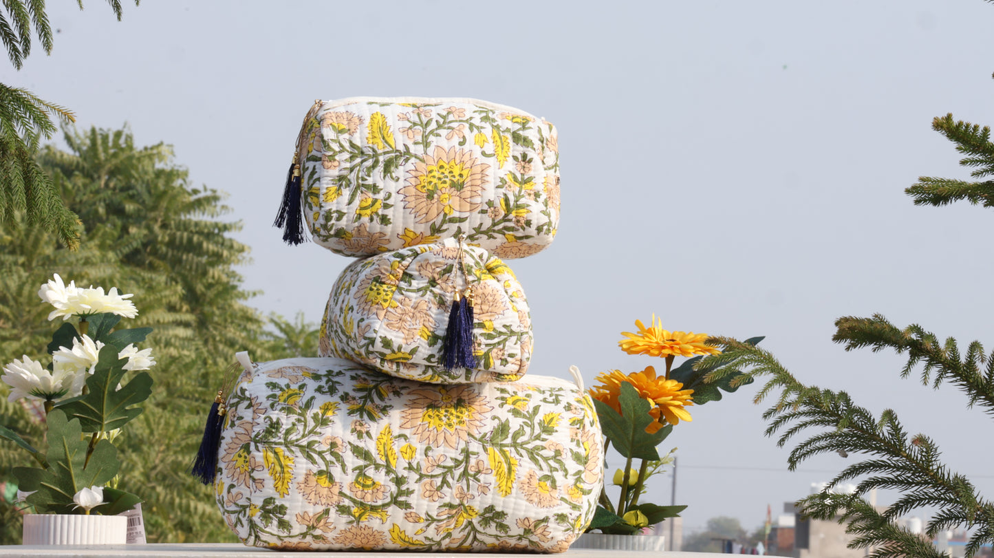 Stack of floral-patterned ottomans with tassels on a rooftop with plants in the background