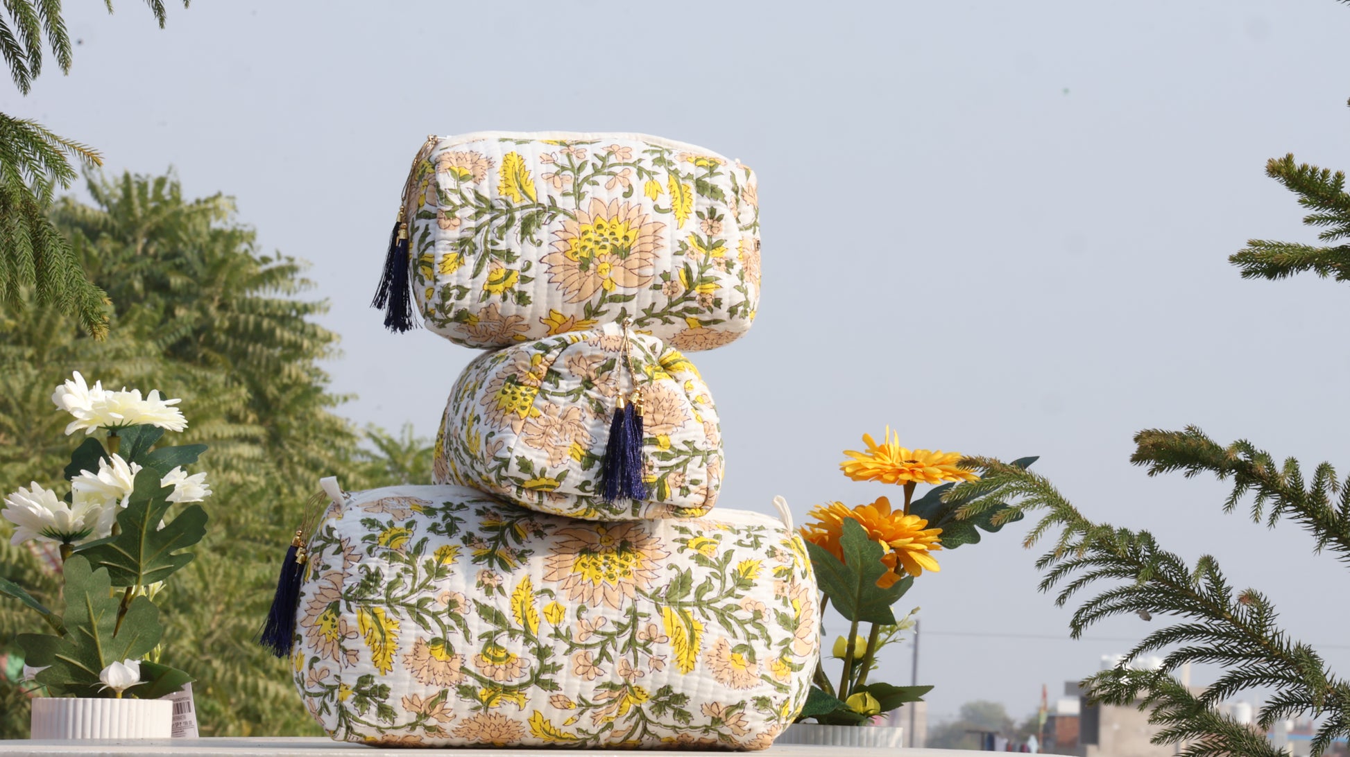 Stack of floral-patterned ottomans with tassels on a rooftop with plants in the background