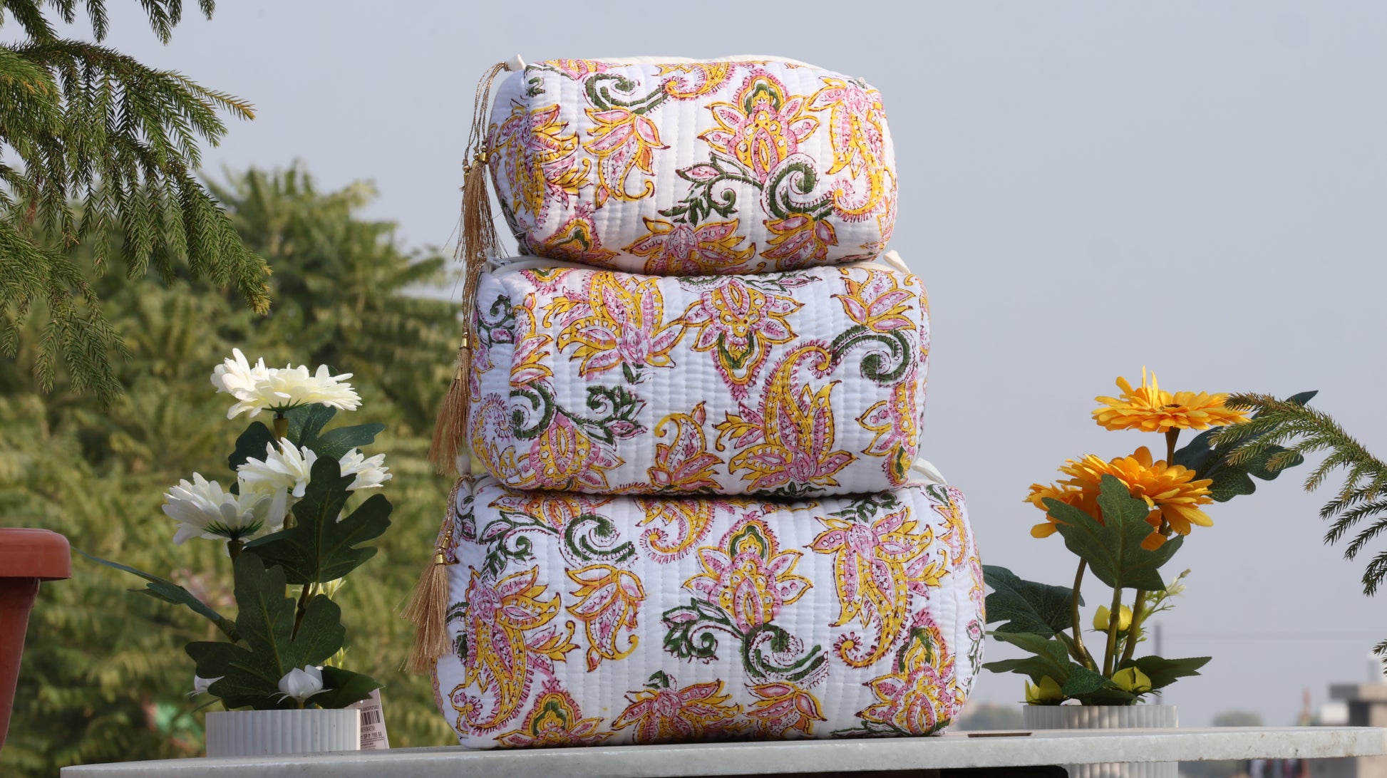Stack of patterned fabric bags on a table with plants in the background