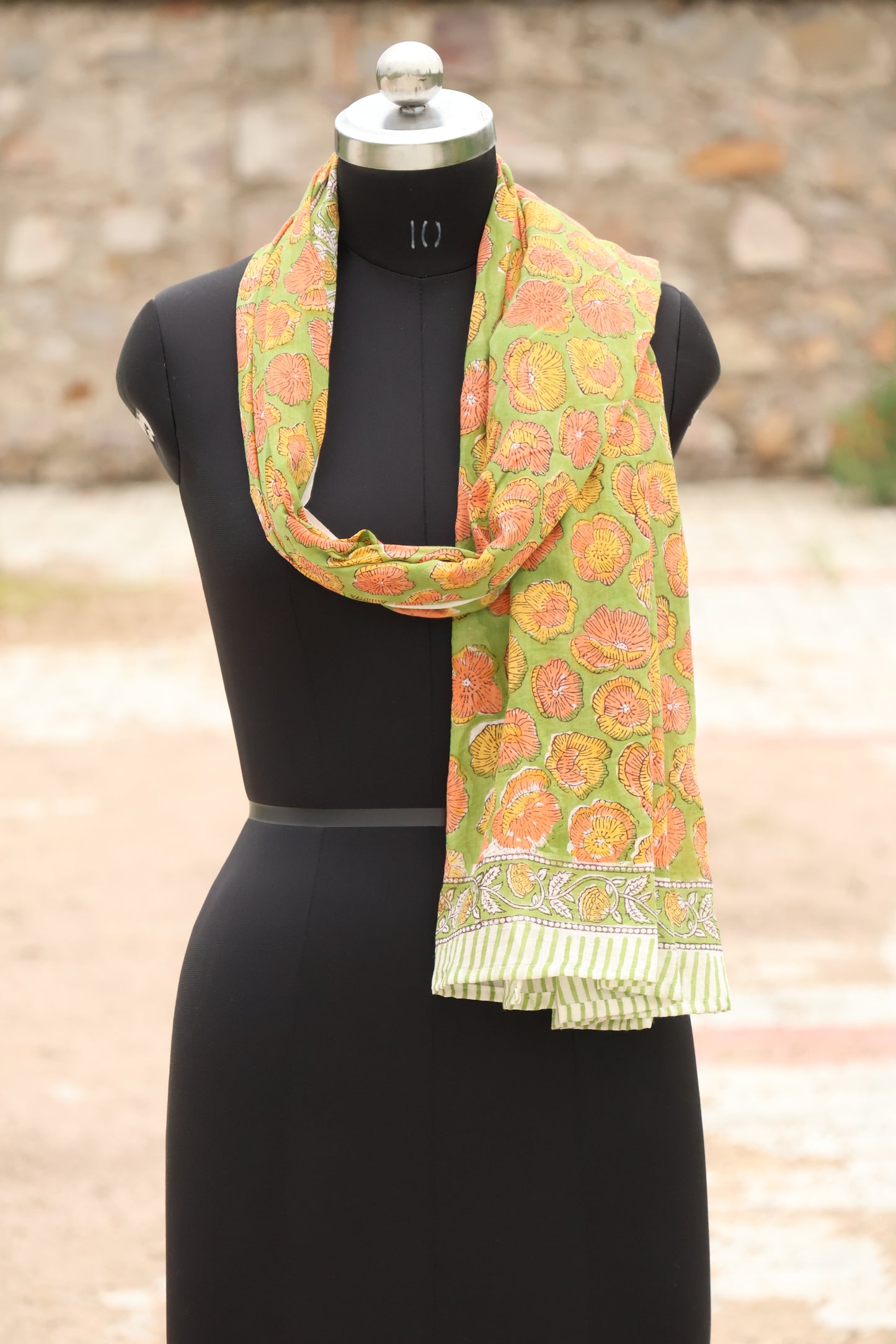 Mannequin wearing a green floral scarf with a blurred outdoor background
