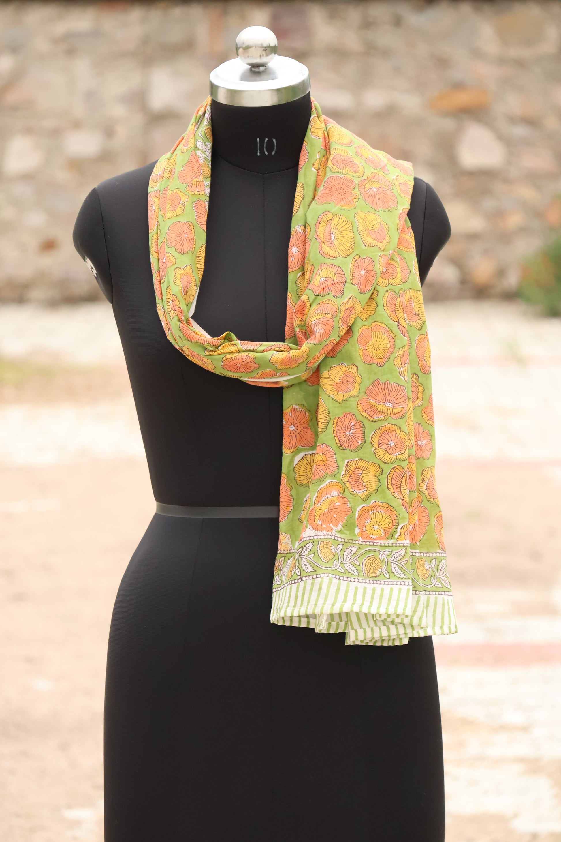 Mannequin wearing a green floral scarf with a blurred outdoor background