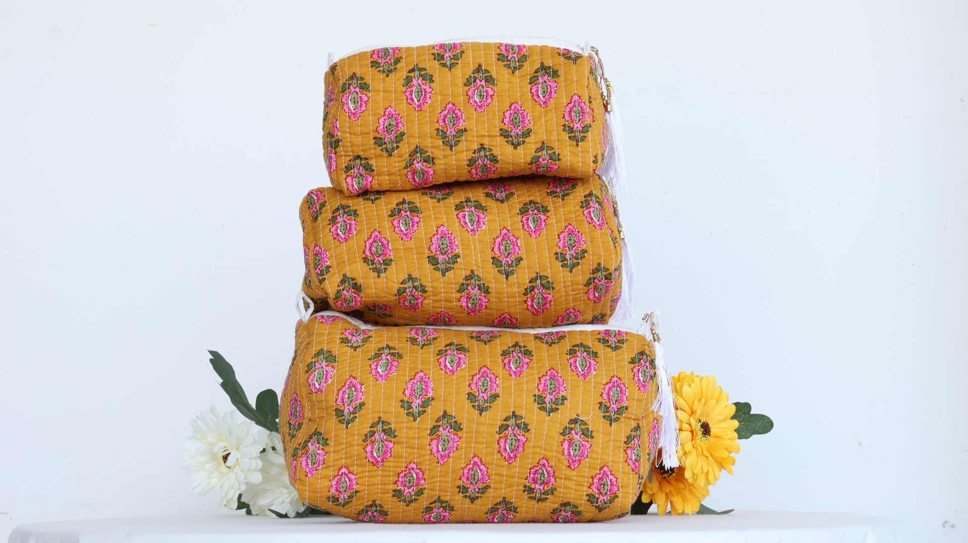 Stack of three yellow floral-patterned makeup bags with a white background