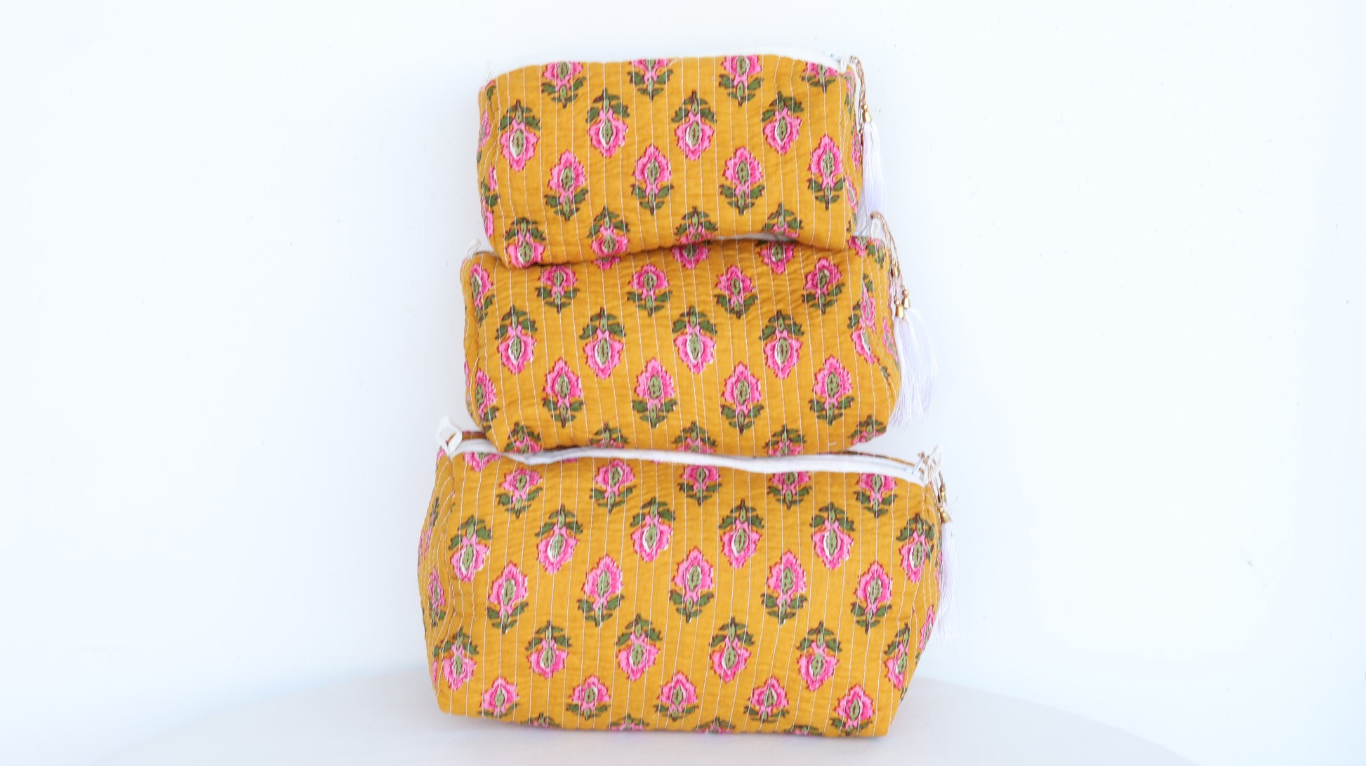 Set of three yellow fabric bags with pink floral patterns on a white background
